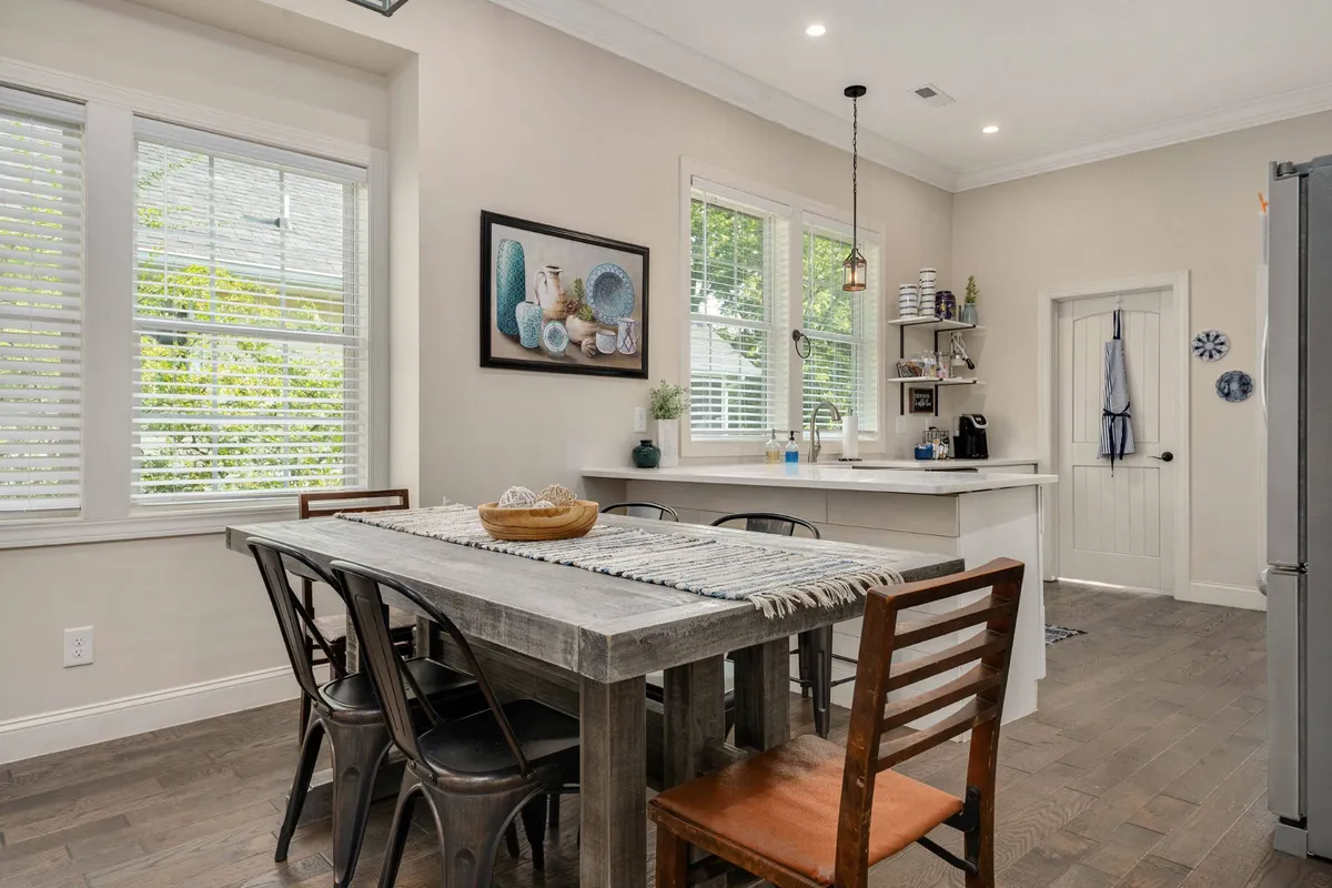 A welcoming dining area featuring a large dining table set for several people, wall art, and an adjacent kitchen counter. The space is designed to bring people together for meals and celebrations, blending seamlessly with the living areas.