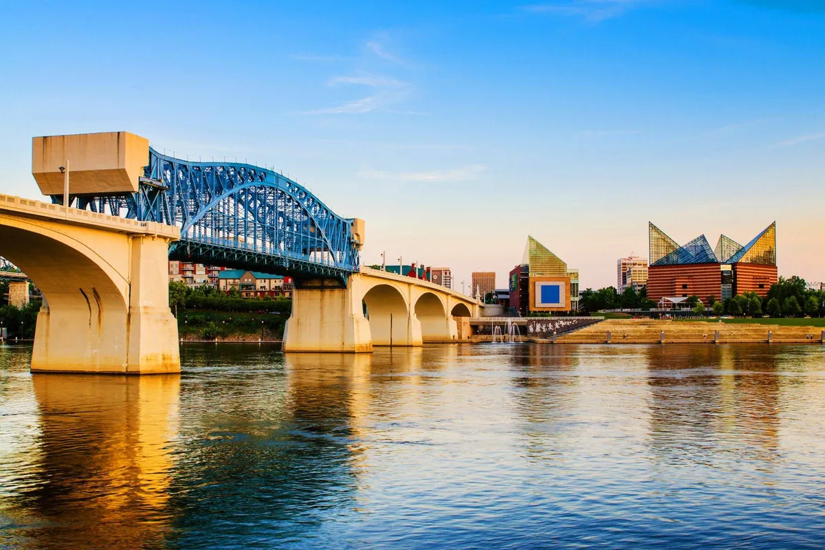 The image captures a scenic view of a blue arch bridge, modern buildings, and a reflective river surface—evoking the proximity to riverwalks and the vibrant local area mentioned in the text.