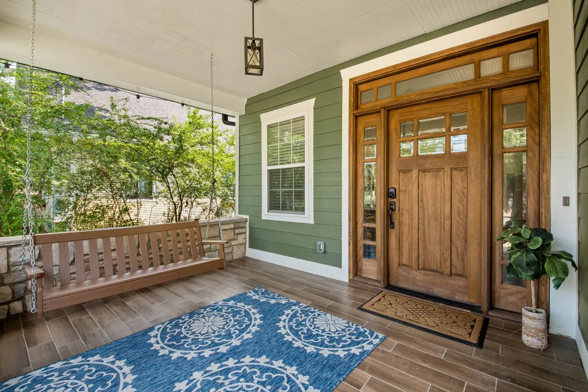 A welcoming front porch with a wooden front door, a hanging swing, decorative rug, and a potted plant. The porch is bathed in natural light and conveys a sense of comfort and hospitality, with inviting outdoor seating—ideal for relaxing with your dog after city adventures.