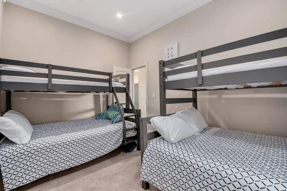 The image captures a playful and relaxed bunk room, furnished with twin-over-full bunk beds, textured bedding, and fun decorative wall art. The space feels adaptable, perfect for both children and adults, inviting late-night chats, play, and relaxation.