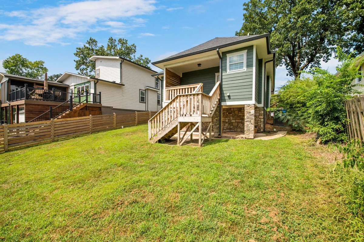 A cheerful scene featuring wooden steps leading to the porch, a green exterior, a well-maintained lawn, and glimpses of neighboring houses. Children playing and opportunities for gatherings are suggested by the space.
