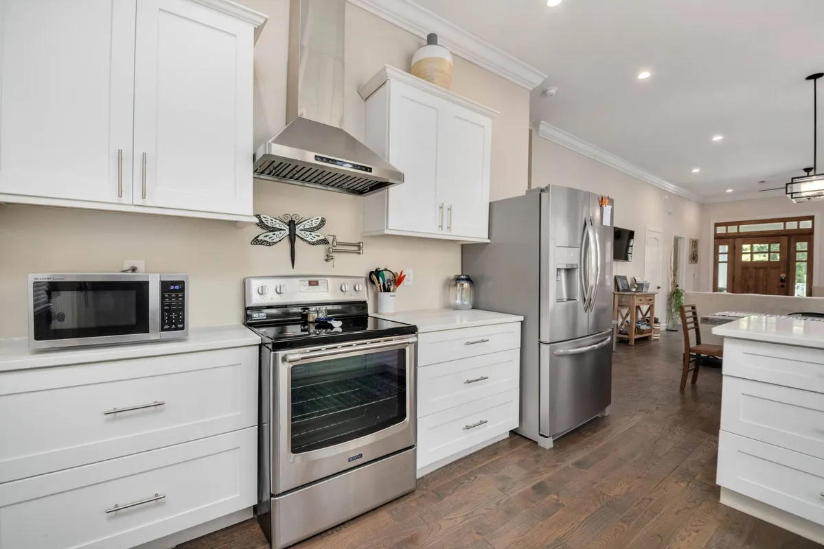 A modern kitchen with stainless steel appliances, white cabinetry, wooden flooring, and decorative wall art. The layout is open and functional, perfect for casual breakfasts at the kitchen bar or helping out with meal prep.