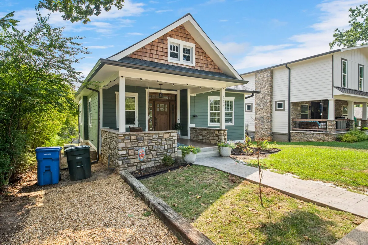 Featuring the home's front porch with stone foundation, shingle roof, and lush green siding, this image conveys a welcoming entrance—ideal for relaxing or gathering before heading out to explore.