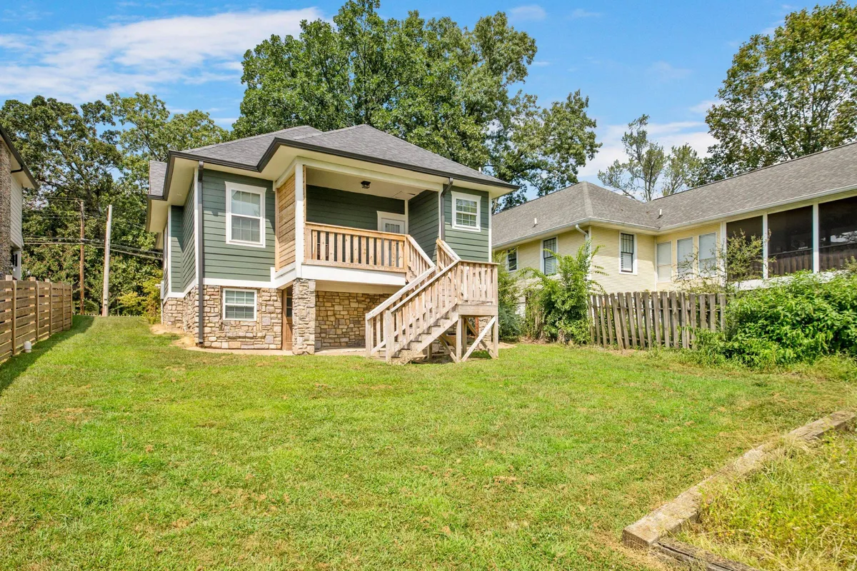 A wide view of the front porch and staircase leading to a green grass lawn, framed by tall trees. The expansive, unfenced backyard provides space for children to play and dogs to explore, while the porch serves as a welcoming hub for gatherings.