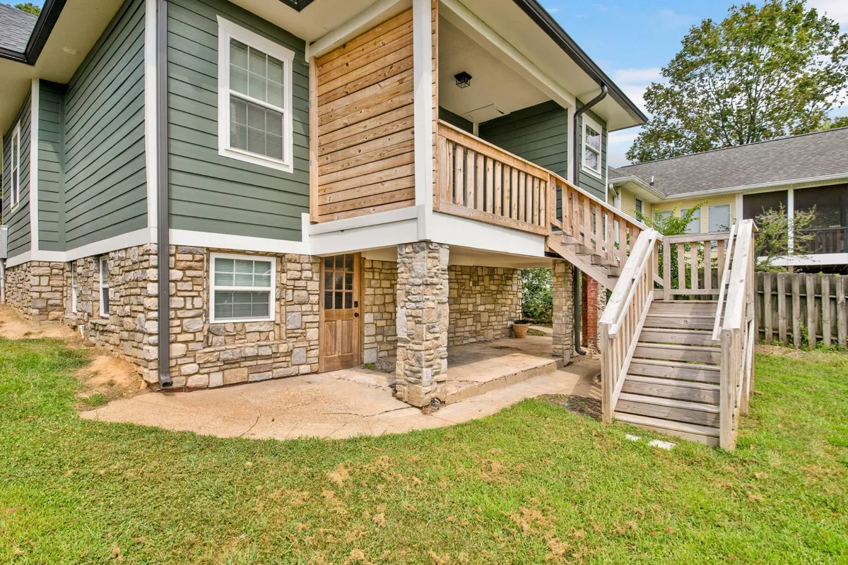 This image showcases the inviting exterior of the Swallowtail, with a stone foundation, wooden balcony, and green siding. The outdoor space is designed for relaxation and gatherings, suggesting the ideal setting for morning coffee or group barbecues.