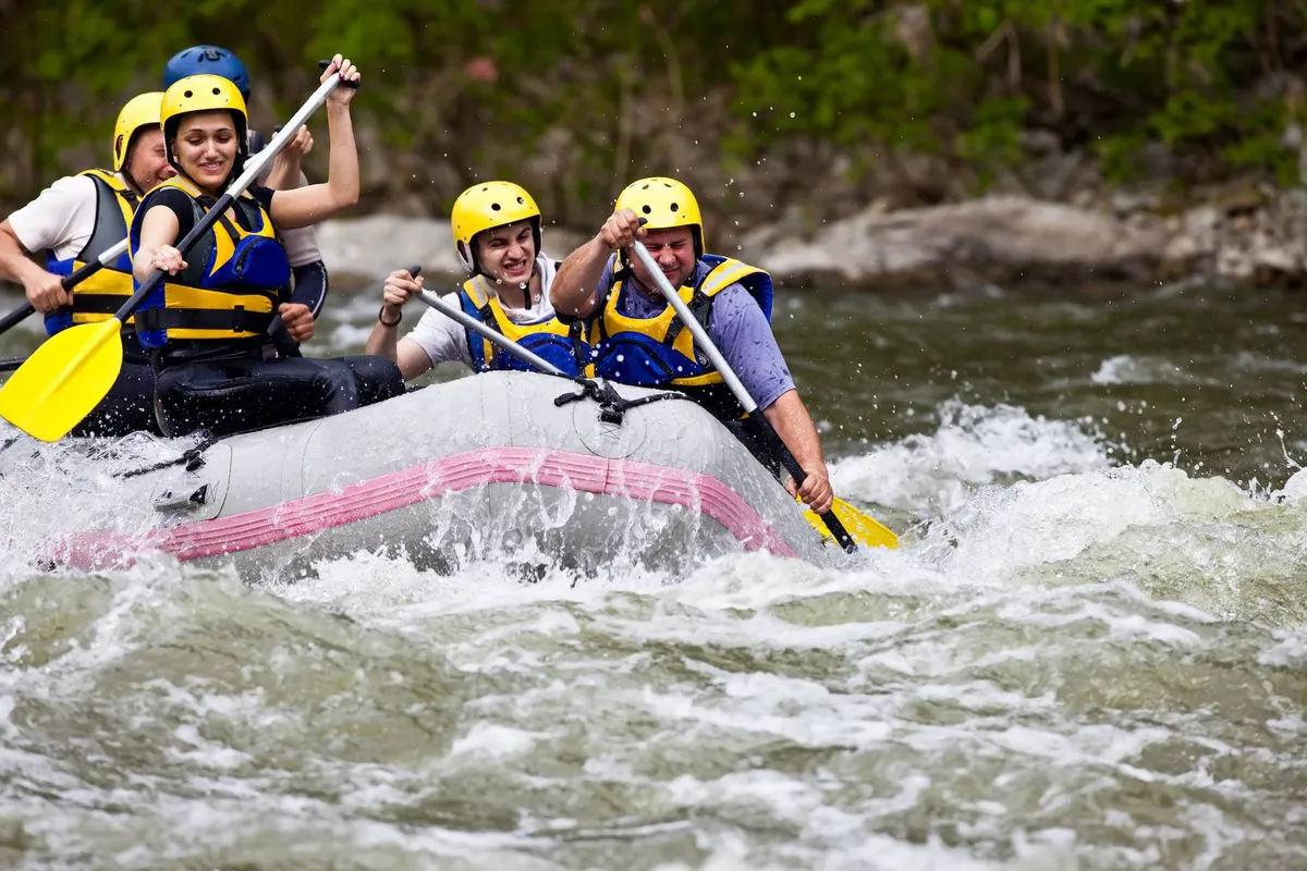 A rafting boat filled with participants paddling down a lively river, surrounded by lush greenery. The scene is active and energetic, highlighting the area’s adventurous spirit and group-friendly outdoor activities.