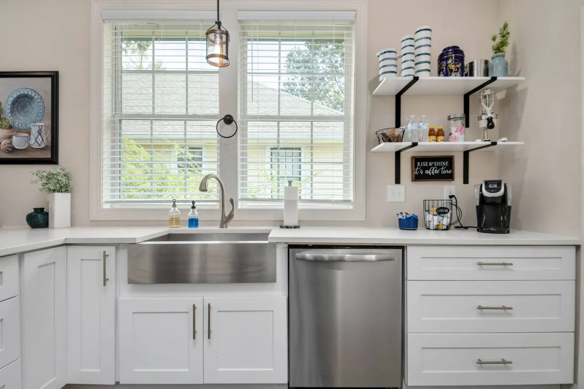 A welcoming kitchen scene highlighting a large stainless steel sink, contemporary faucet, open shelves with decorative items, and a coffee maker setup. The arrangement suggests an inviting space for both meal prep and enjoying a morning coffee ritual.